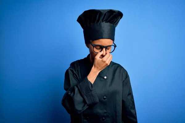 Young african american chef woman wearing cooker uniform and hat over blue background tired rubbing nose and eyes feeling fatigue and headache. Stress and frustration concept.