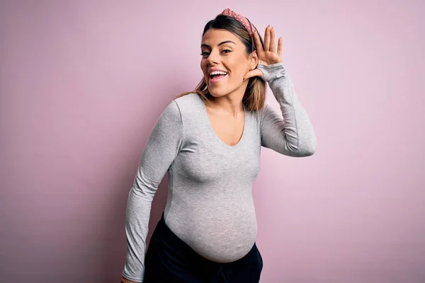 孤立したピンクの背景の上に赤ちゃんを期待若い美しいブルネットの女性は噂やゴシップへの聴聞会を聞いて手で笑みを浮かべて 病気の概念 — ストック写真
