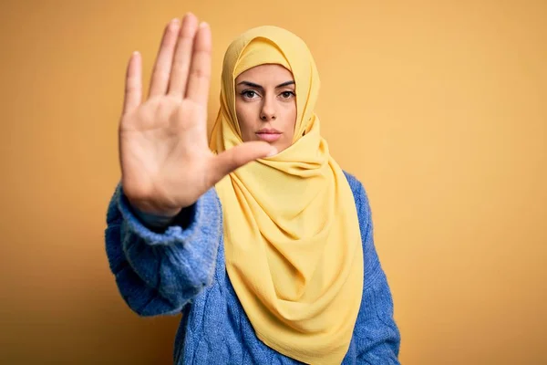 年轻美丽的黑发穆斯林女子 头戴阿拉伯头巾 头戴黄褐色背景的头巾 手掌心停止歌唱 脸上带有消极而严肃的手势的警告表情 — 图库照片