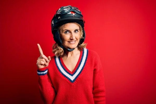 中世の美しいブロンドのオートバイの女性は 成功したアイデアで指を指す赤い背景の上に元ヘルメットを身に着けています 興奮し 第一番 — ストック写真