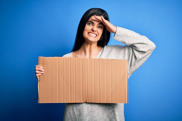 Young beautiful brunette activist woman holding blank cardboard banner protesting stressed with hand on head, shocked with shame and surprise face, angry and frustrated. Fear and upset for mistake.