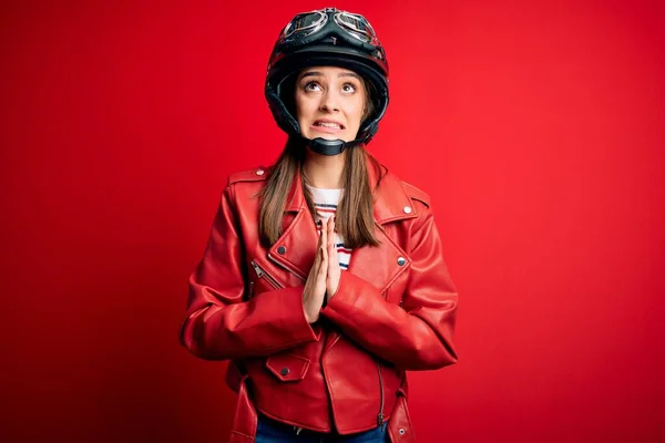 オートバイのヘルメットと赤いジャケットを身に着けている若い美しいブルネットの元サイクリストの女性は 非常に感情的で心配している顔に希望の表情と一緒に手で物乞いと祈ります 物乞い — ストック写真