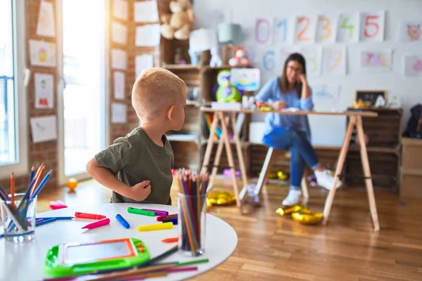 若い白人の子供は教師と一緒に学校で遊んでいる 母と息子は遊び場で色鉛筆で絵を描く若い女性は机の上に座っている — ストック写真