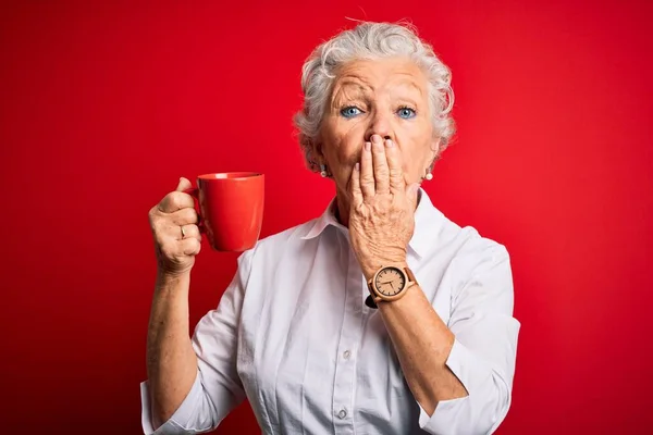 年长美丽的女人站在孤立的红底封口上喝着一大杯咖啡 手被错误 恐惧的表情 沉默中的恐惧 神秘的概念所震惊 — 图库照片