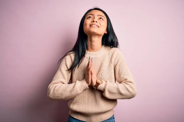 Young beautiful chinese woman wearing casual sweater over isolated pink background begging and praying with hands together with hope expression on face very emotional and worried. Begging.