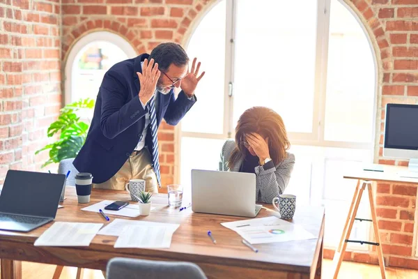 Two middle age business workers working together. Man bullying woman at the office