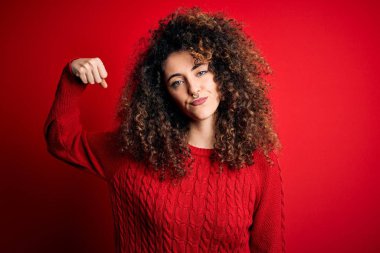 Kıvırcık saçlı, sıradan kırmızı kazak giyen güçlü kol kaslı, kendinden emin ve gururlu bir kadın.