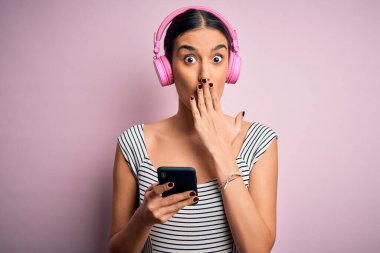 Genç, güzel, esmer bir kadın müzik dinliyor kulaklık ve akıllı telefon kullanıyor. Ağzını kapatıyor. Utancından ağzı açık kalıyor.