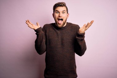 Sarışın, sakallı ve mavi gözlü genç adam pembe arka planda sıradan bir süveter giyiyor. Çılgınlığı kutluyor ve başarını kutluyor. Kolları havada ve gözleri açık, heyecanlı bir şekilde çığlık atıyor. Kazanan konsept