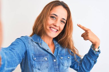 Genç kızıl saçlı kadın izole edilmiş arka planda selfie çekiyor. Elle ve parmakla işaret ederek çok mutlu.