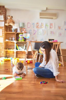Anaokulundaki bir sürü oyuncağın etrafında dijital tahta kullanarak güzel öğretmen ve bebek çizimi yapıyorlar.