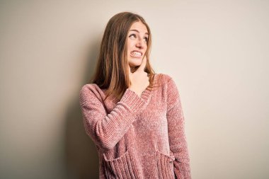 Genç, güzel, kızıl saçlı, pembe bir süveter giyen, soyutlanmış beyaz arka planda bir soru hakkında endişeli, endişeli ve gergin bir kadın.