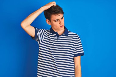 Teenager boy wearing casual t-shirt standing over blue isolated background confuse and wondering about question. Uncertain with doubt, thinking with hand on head. Pensive concept. clipart