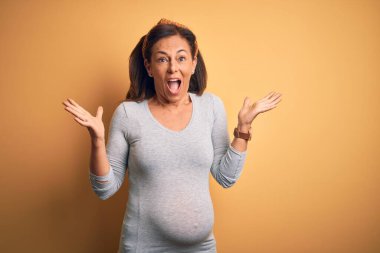 Orta yaşlı hamile bir kadın hamile. Hamileliğini çılgınca kutluyor ve başarıya hayret ediyor. Kolları açık, gözleri açık, heyecanlı bir şekilde bağırıyor. Kazanan konsept