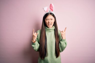 Pembe arka planda sevimli paskalya tavşanı kulakları takan genç Asyalı bir kadın çılgın bir ifadeyle elleri havada rock sembolü yaparak bağırıyor. Müzik yıldızı. Ağır konsept.