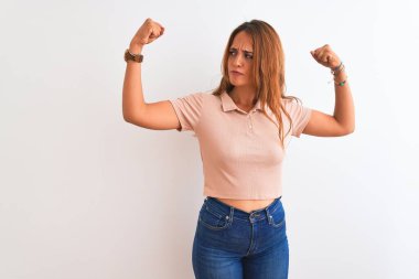 Genç kızıl saçlı kadın, izole edilmiş beyaz arka planda gururla gülümseyen kol kaslarını gösteriyor. Fitness konsepti.