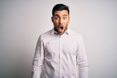 Zarif bir gömlek giyen yakışıklı bir adam izole edilmiş beyaz arka planda korku ve şaşkınlık dolu bir ifade, korku ve heyecan dolu bir yüz..