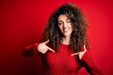 Kıvırcık saçlı, sıradan kırmızı kazak giyen, kendine güvenen, kendini gururlu ve mutlu gösteren genç ve güzel bir kadın..