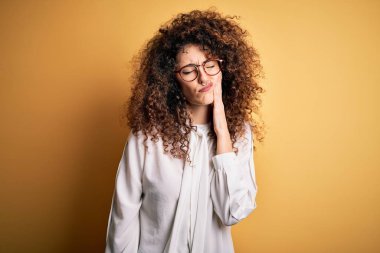 Kıvırcık saçlı, piercingli, tişörtlü, gözlüklü, dişlerinde diş ağrısı ya da diş ağrısı yüzünden elleriyle dudaklarına dokunan güzel esmer bir kadın. Dişçi