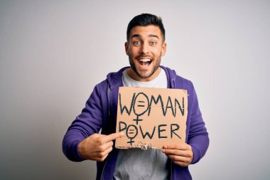Young handsome activist man protesting for woman power holding cardboard banner very happy pointing with hand and finger clipart