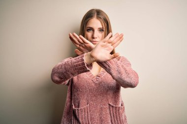 Genç, güzel, kızıl saçlı, pembe kazak giyen, izole edilmiş beyaz arka planda reddedilmiş, kollarını ve avuç içlerini çaprazlayan, negatif işaret veren, kızgın yüzlü bir kadın.