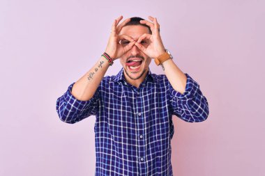 Tecrit edilmiş arka planda duran yakışıklı genç adam dürbün gibi jest yapıyor. Dürbün dilini çıkarıyor, gözler parmaklarından bakıyor. Çılgın ifade.