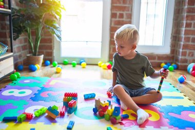 Anaokulunda oyuncak bloklarıyla oynayan beyaz bir çocuk. Anaokulu çocuğu oyun odasında kule inşa etmekten mutlu.