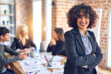 Birlikte çalışan bir grup işçi. Genç ve güzel bir kadın gülümsüyor, mutlu bir şekilde büroda kameraya bakıyor.