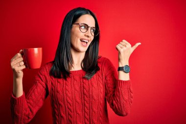 Genç esmer, mavi gözlü, gözlüklü, kahve içen ve gülümseyen bir yüzü olan bir kadın.