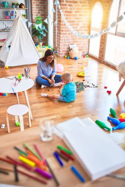 Genç beyaz çocuk öğretmeniyle oyun okulunda oynuyor. Anne ve oğlu oyun odasında oyuncak blokları olan bir kuleyi şişiriyorlar.