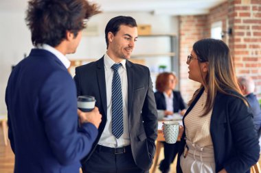 Mutlu ve kendinden emin bir şekilde gülümseyen genç ve güzel iş adamları kahve içip ofiste konuşuyorlar.