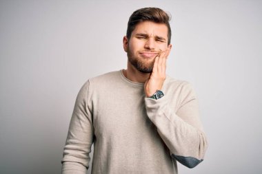 Sakallı ve mavi gözlü genç sarışın adam diş ağrısı ya da diş hastalığından dolayı elleri ve elleri ağrıyan ağızlarına dokunan sıradan bir kazak giyiyor. Dişçi