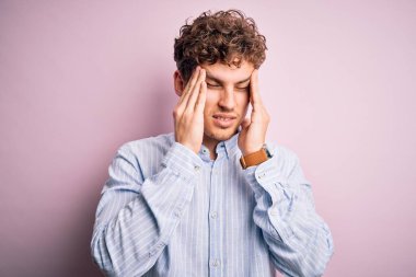 Sarışın, kıvırcık saçlı, beyaz arka planda çizgili gömlek giyen ve stresten dolayı baş ağrısı çeken genç bir adam. Migren ağrısı..