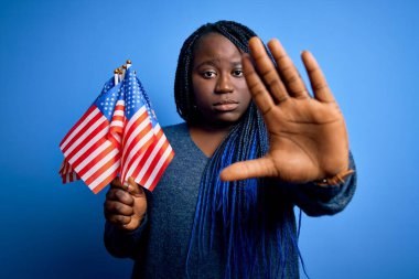 Genç vatansever Afro-Amerikalı örgülü kadın elinde Birleşik Devletler bayrakları var dur işareti yapıyor ciddi ve kendinden emin bir ifadeyle, savunma jesti