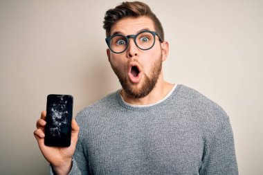 Sakallı, mavi gözlü, gözlüklü, kırık akıllı telefon takan, şaşırmış, korkmuş ve korku ifadesinden heyecanlanan genç sarışın bir adam.