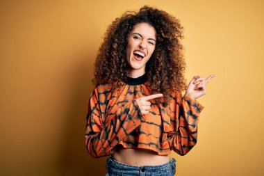 Kıvırcık saçlı, piercingli, sıradan tişörtlü, gülümseyen ve kameraya bakan genç, güzel esmer kadın..