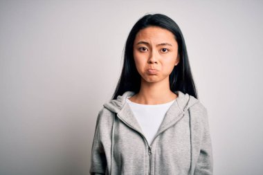 Genç, güzel, Çinli sporcu kadın, izole edilmiş beyaz arka planda eşofman üstü giyiyor. Depresyonda ve endişe içinde, kızgın ve korkmuş bir halde. Üzücü ifade.