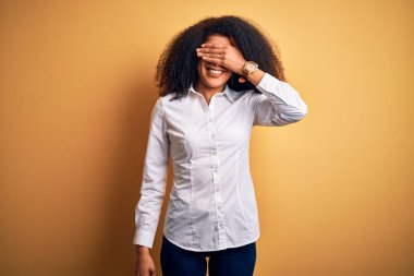 Afro saçlı, sarı arka planda dikilen güzel Afro-Amerikan zarif genç bir kadın. Gülümsüyor ve yüzünde şaşkınlıktan gözleri kapayarak gülüyor. Kör kavram.