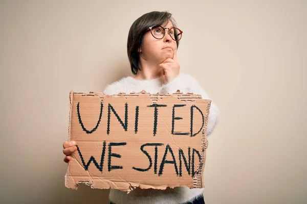 Young down syndrome woman holding protest banner with united we stand rights message serious face thinking about question, very confused idea