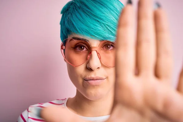 Young beautiful woman with blue fashion hair wearing fanny glasses with hearts with open hand doing stop sign with serious and confident expression, defense gesture