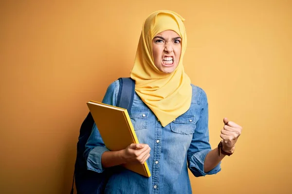 年轻的女学生头戴穆斯林头巾 背着背包 背着黄色背景的书 怒气冲冲地大叫 疯狂地高喊 怒气冲冲 — 图库照片