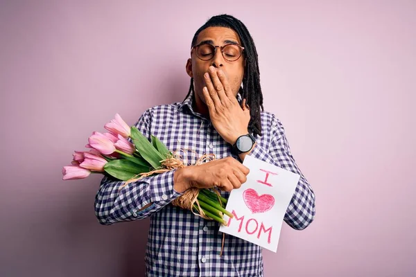 African american man with dreadlocks holding love mom message and tulips on mothers day cover mouth with hand shocked with shame for mistake, expression of fear, scared in silence, secret concept