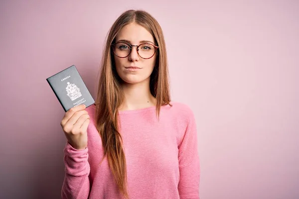 ピンク地の上にカナダのパスポートを保持している美しい赤毛の観光客の女性は真剣に考えてスマート顔に自信を持って式で — ストック写真