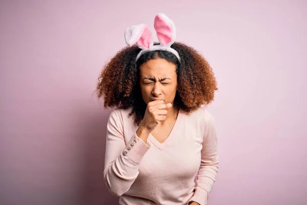 ピンクの背景にウサギの耳を身に着けているアフロヘアを持つ若いアフリカ系アメリカ人女性は具合が悪く 風邪や気管支炎の症状として咳をする ヘルスケアの概念 — ストック写真