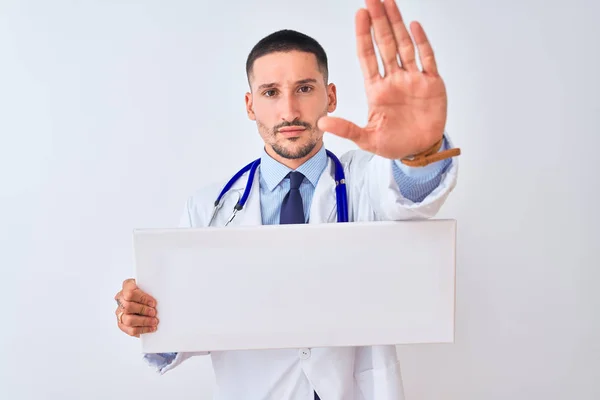年轻的医生举着空白的广告横幅 高举孤立的背景 张开双手 用严肃而自信的表情 做了个手势 做了个防守动作 — 图库照片