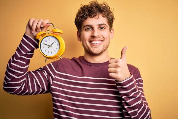 Joven Hombre Rubio Con Pelo Rizado Sosteniendo Reloj Despertador Pie —  Fotos de Stock