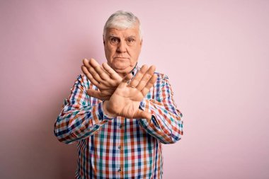 Kıdemli yakışıklı, beyaz gömlekli, pembe arka planda yalnız bırakılmış, reddedilmiş, kollarını kavuşturmuş, negatif işaret veren, kızgın yüzlü adam.