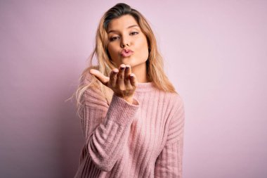 İzole edilmiş arka planda pembe süveter giyen genç, güzel, sarışın bir kadın havayla öpüşen kameraya bakıyor. Güzel ve seksi. Aşk ifadesi.