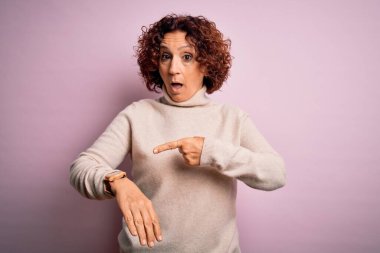 Orta yaşlı, kıvırcık saçlı, pembe arka plan üzerine normal balıkçı yaka kazak giyen güzel bir kadın.