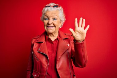 Son sınıf güzeli, gri saçlı, günlük kırmızı ceket giyen, güneş gözlüklü, dört numarayı gösteren ve gülümseyen, kendinden emin ve mutlu bir kadın..